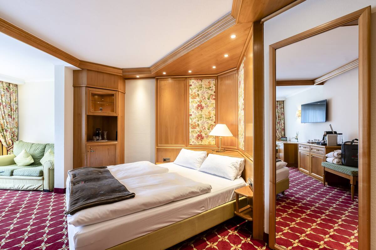 A hotel room with a large bed, wooden wardrobe, a desk with a lamp, and a television.