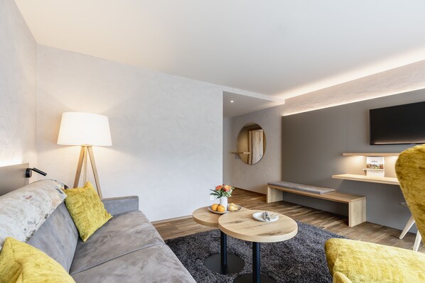 Una sala de estar moderna con un sofá gris, cojines amarillos, una mesa redonda de madera y una lámpara.