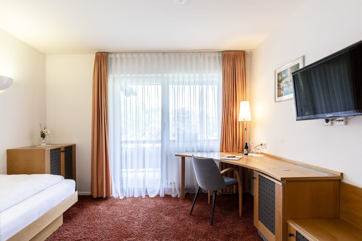 A hotel room with a bed, desk, chair, TV, and a window with curtains.