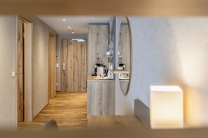 A modern hotel hallway with wooden flooring, a mirror, and a counter with amenities.