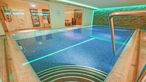 An indoor swimming pool with clear glass walls, a tiled floor, and a brick wall. - Hotel Restaurant Waldsägmühle (Pfalzgrafenweiler)