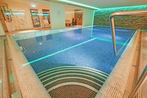 An indoor swimming pool with clear glass walls, a tiled floor, and a brick wall.