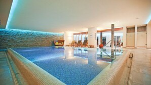 An indoor swimming pool with a tiled floor, lounge chairs, and a brick wall. - Hotel Restaurant Waldsägmühle (Pfalzgrafenweiler)
