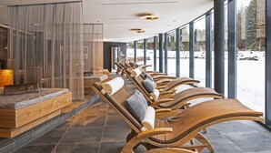 A row of wooden loungers with cushions, a wooden bench, and a glass partition with sheer curtains. - Hotel Restaurant Waldsägmühle (Pfalzgrafenweiler)