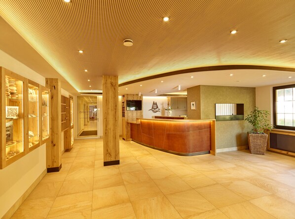 A hotel reception area with a wooden reception desk, a large mirror, and a plant. - Hotel Restaurant Waldsägmühle (Pfalzgrafenweiler)