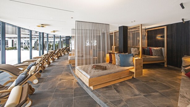 A modern spa area with wooden loungers, a small wooden bed, and a large window offering a view of the outdoors. - Hotel Restaurant Waldsägmühle (Pfalzgrafenweiler)