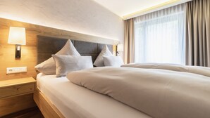 A hotel room with a large bed, a wooden headboard, a nightstand with a lamp, and a window with curtains. - Hotel Restaurant Waldsägmühle (Pfalzgrafenweiler)