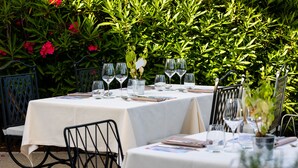 Un área de comedor al aire libre con mesas preparadas para dos, rodeada de exuberante follaje y flores.