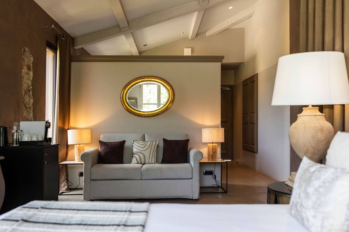 A modern hotel room with a sofa, two bedside lamps, a round mirror, and a bed.