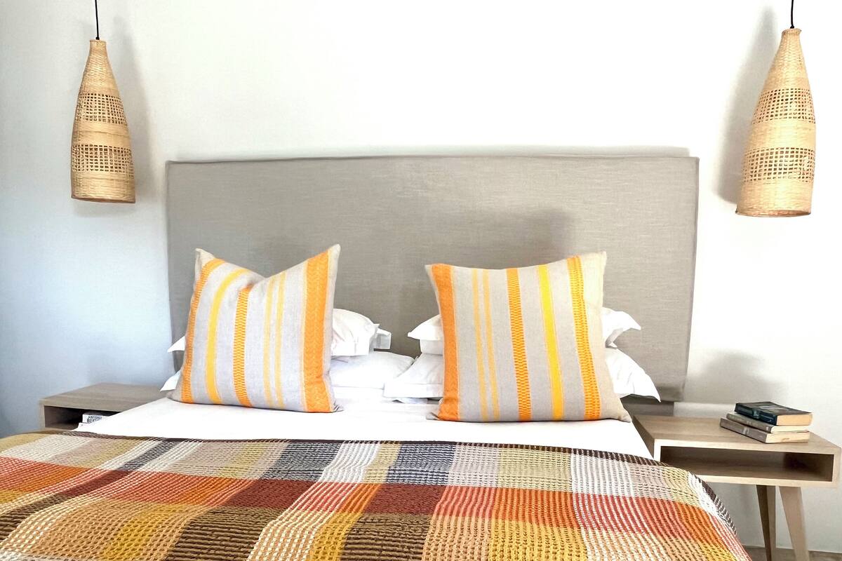 A neatly made bed with striped pillows, a checkered blanket, and two bedside tables with books.