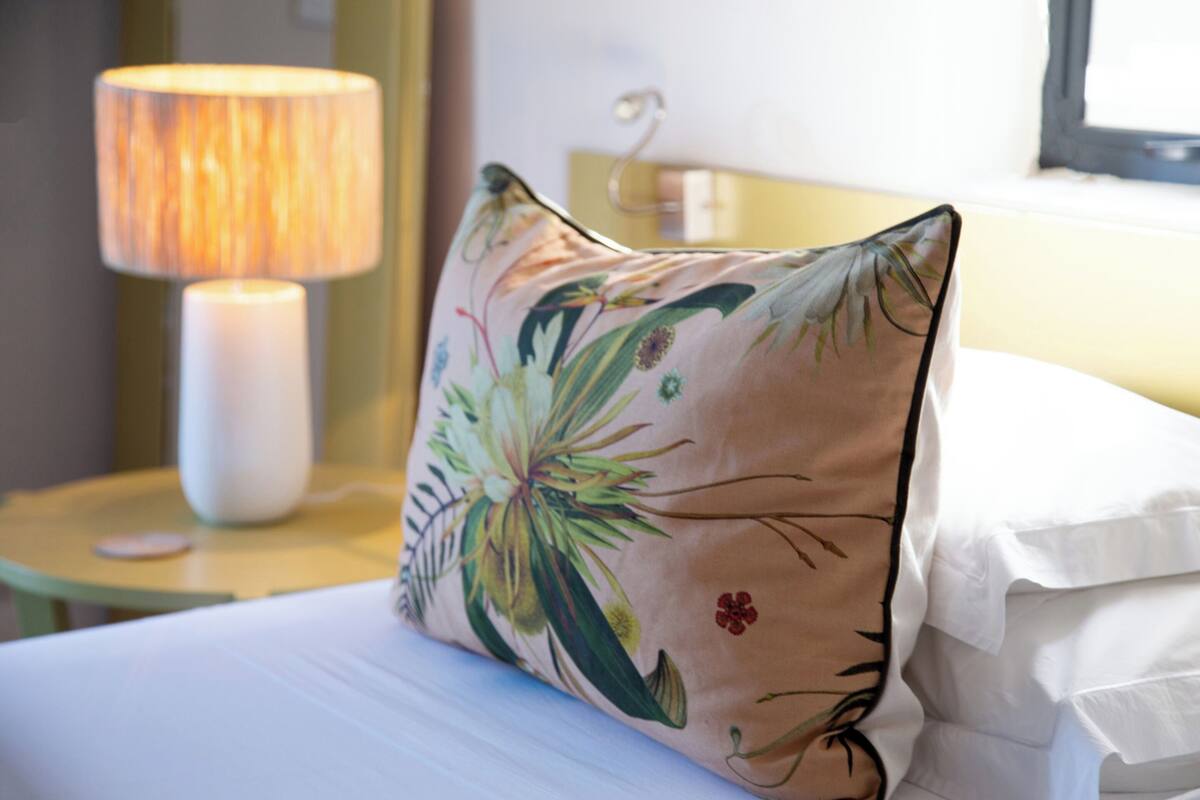 A bed with a floral pillow, a bedside lamp, and a small table with a mouse.