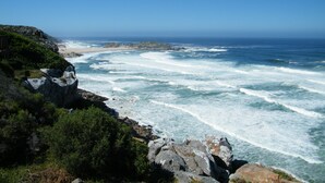 A coastal landscape with rocky cliffs, a sandy beach, and the ocean. - Christiana Lodge (Plettenberg Bay)