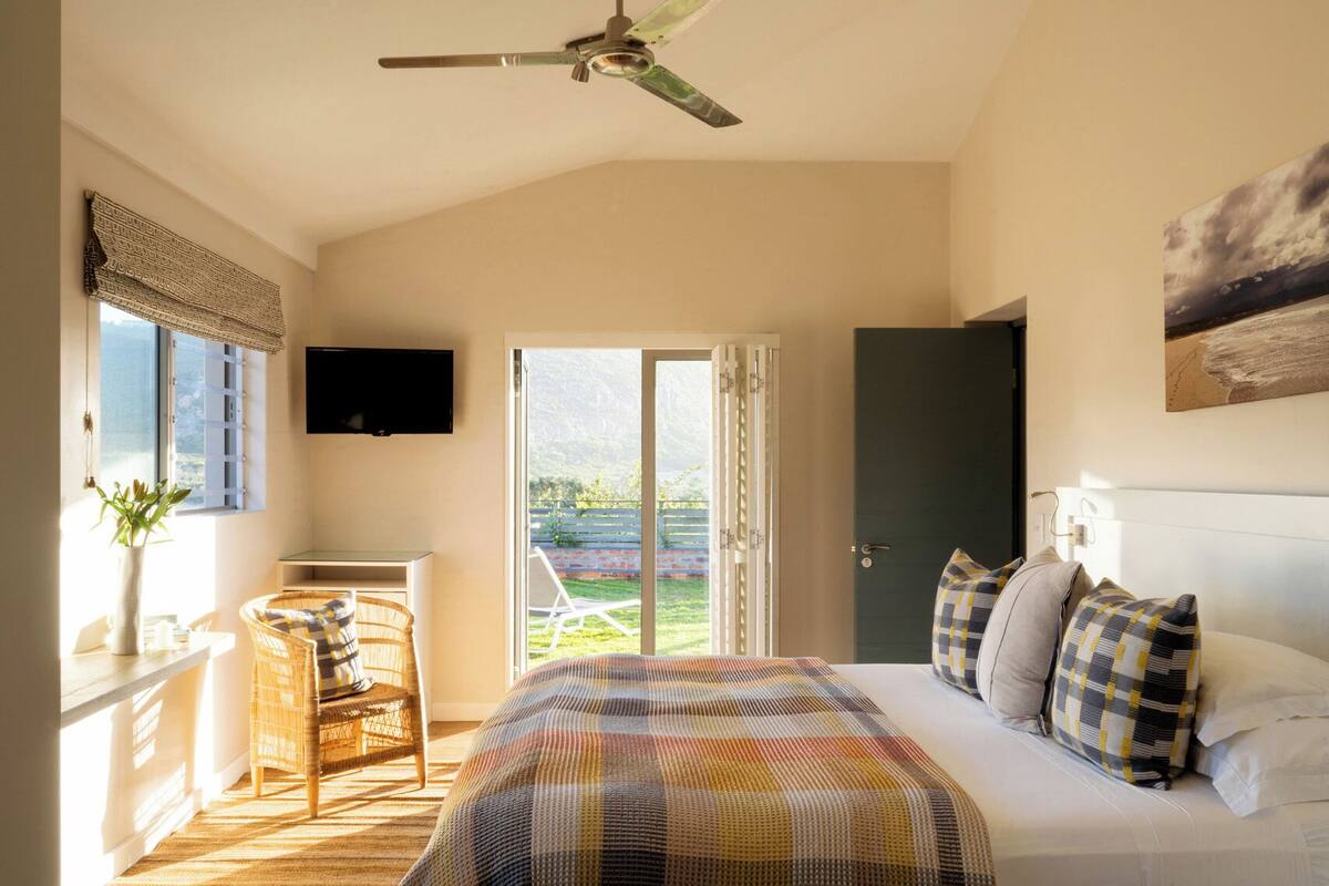 A bedroom with a bed, a television, a wicker chair, a window, and a door leading to a balcony.