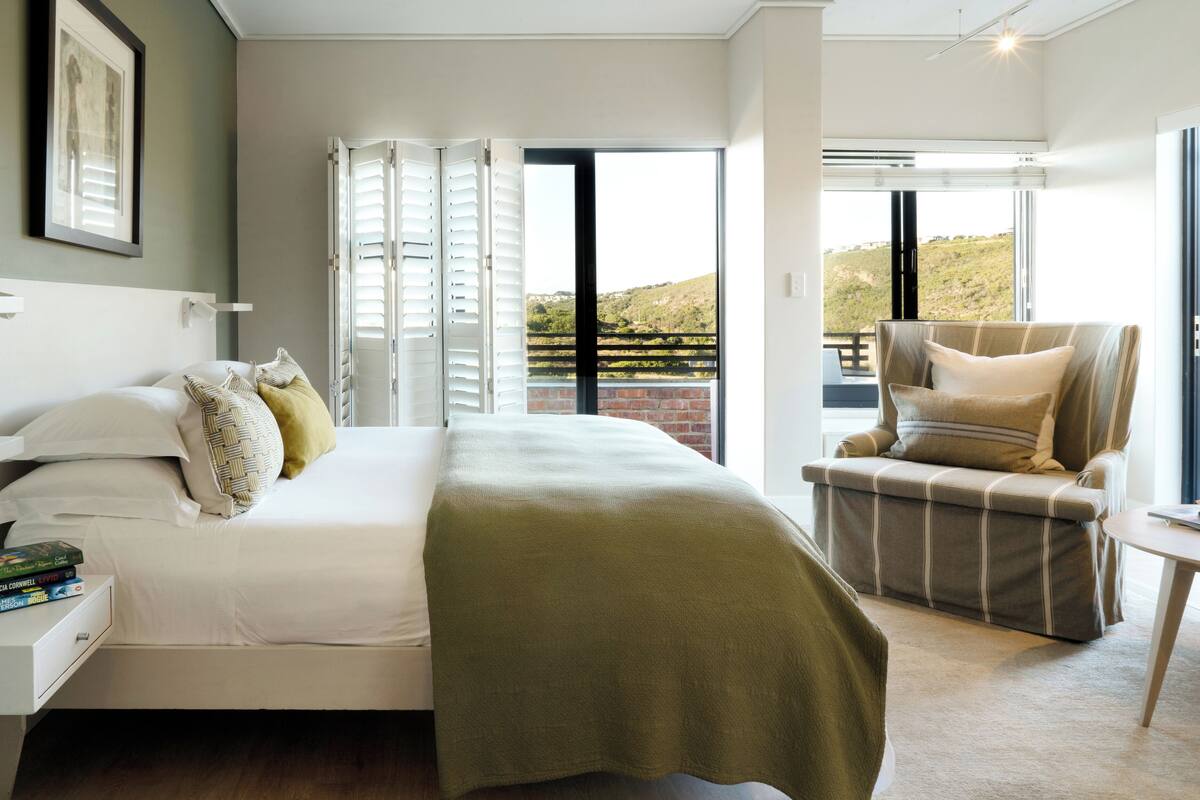 A bedroom with a bed, a chair, and a view of the outdoors.