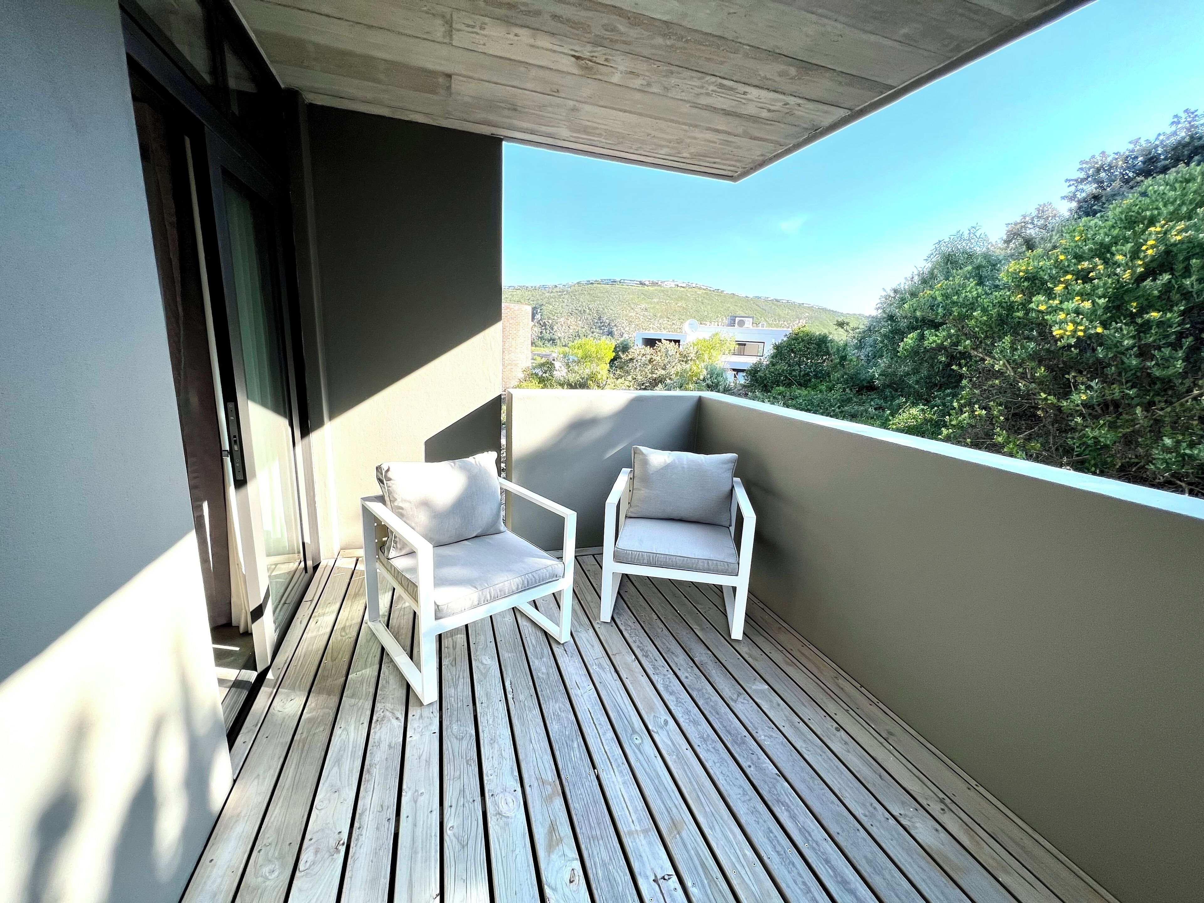 Varanda com duas cadeiras brancas e piso de madeira.