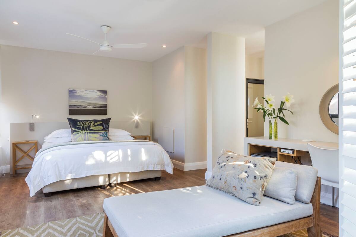 A modern bedroom with a bed, bedside tables, a desk, and a chair.