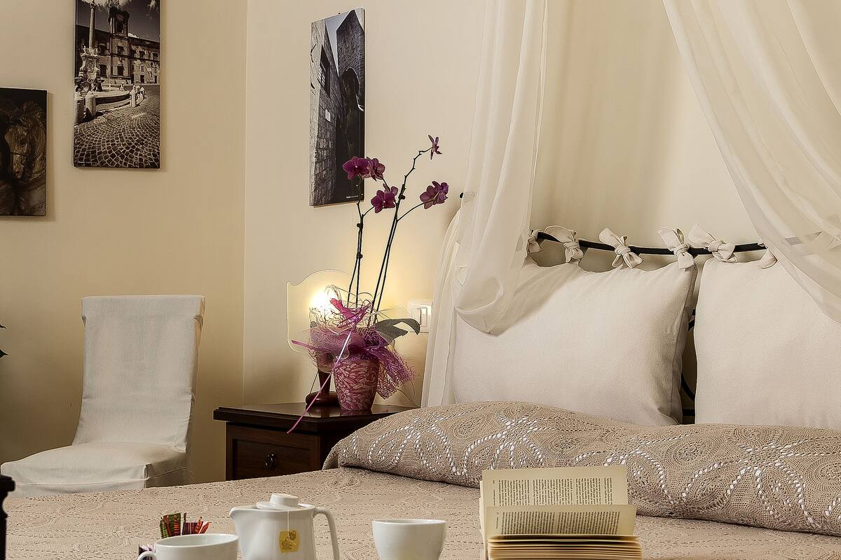 A hotel room with a bed, a chair, a bedside table with a lamp, and artwork on the walls.