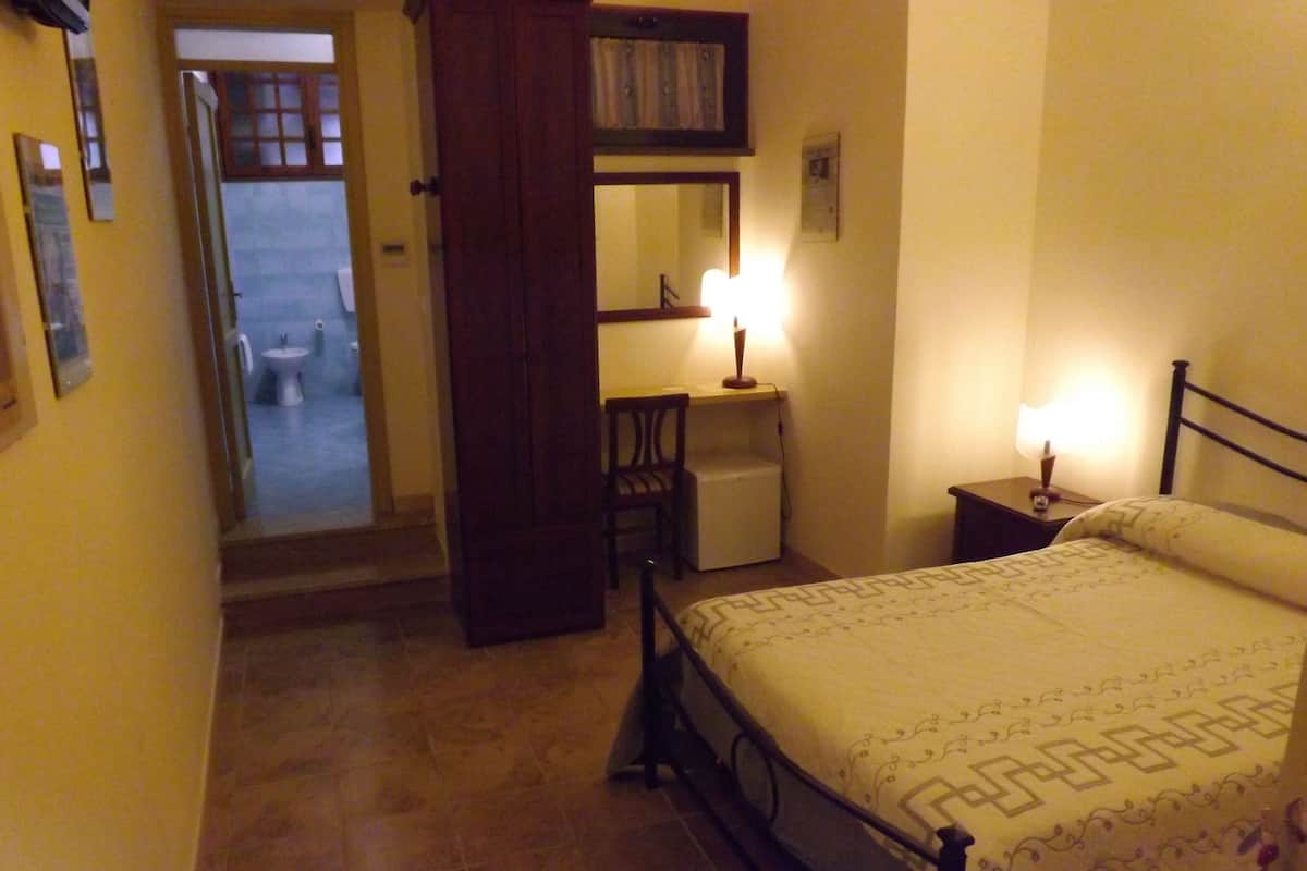 A bedroom with a bed, bedside table, lamp, chair, and a small desk.