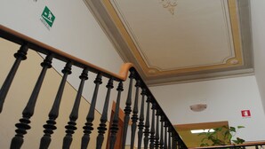 Una escalera con barandillas negras ornamentadas y un techo decorativo con motivos florales.
