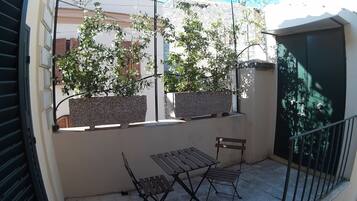 Un balcone con due sedie di legno, un tavolino, piante in vaso e vista sulla città.