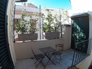 A balcony with two wooden chairs and a small table, potted plants, and a view of the cityscape. - Camere del Re (Tarquinia)