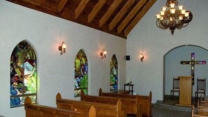 Interior de iglesia con bancos de madera, vidrieras y techo de madera.