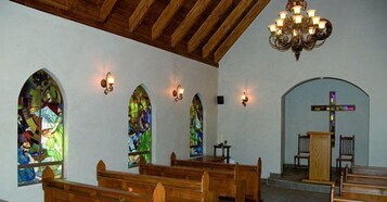 Interior de igreja com bancos de madeira, vitrais e teto de madeira.