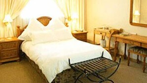 Una habitación de hotel con cama, escritorio, silla, espejo y cortinas.