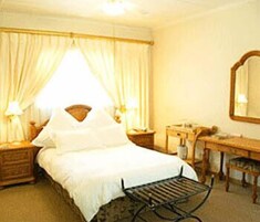 Quarto de hotel com cama, escrivaninha, cadeira, espelho e cortinas.