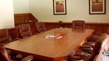 A conference room with a long wooden table, brown leather chairs, and two framed landscape paintings on the wall.