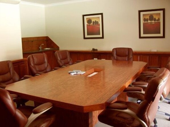A conference room with a long wooden table, brown leather chairs, and two framed landscape paintings on the wall.