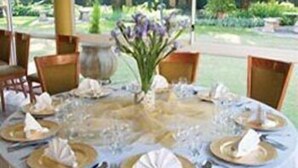 Una mesa redonda dispuesta para una comida, con mantel blanco, platos dorados y cubiertos.