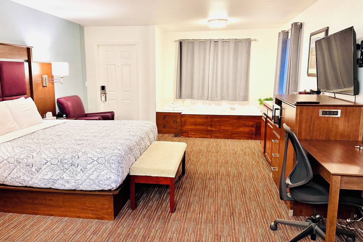 A hotel room with a large bed, a desk with a chair, a small bathroom, and a television.