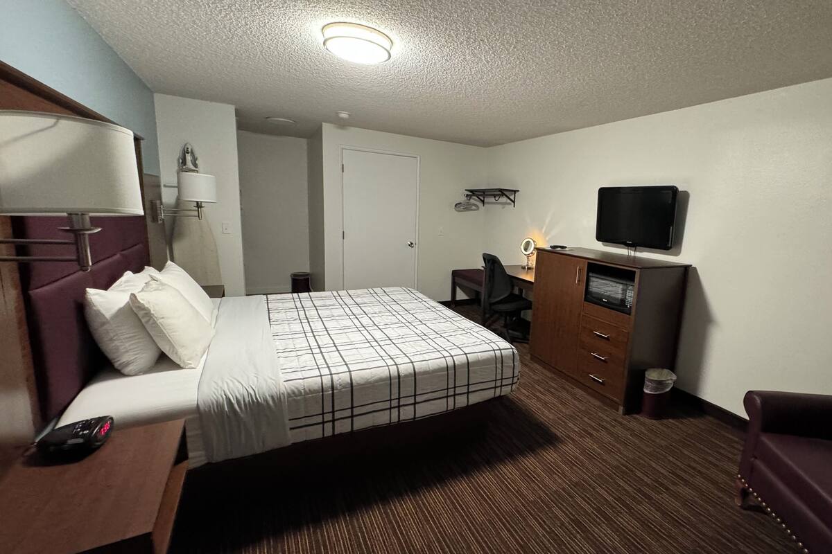 A hotel room with a bed, a desk, a chair, a TV, and a wardrobe.