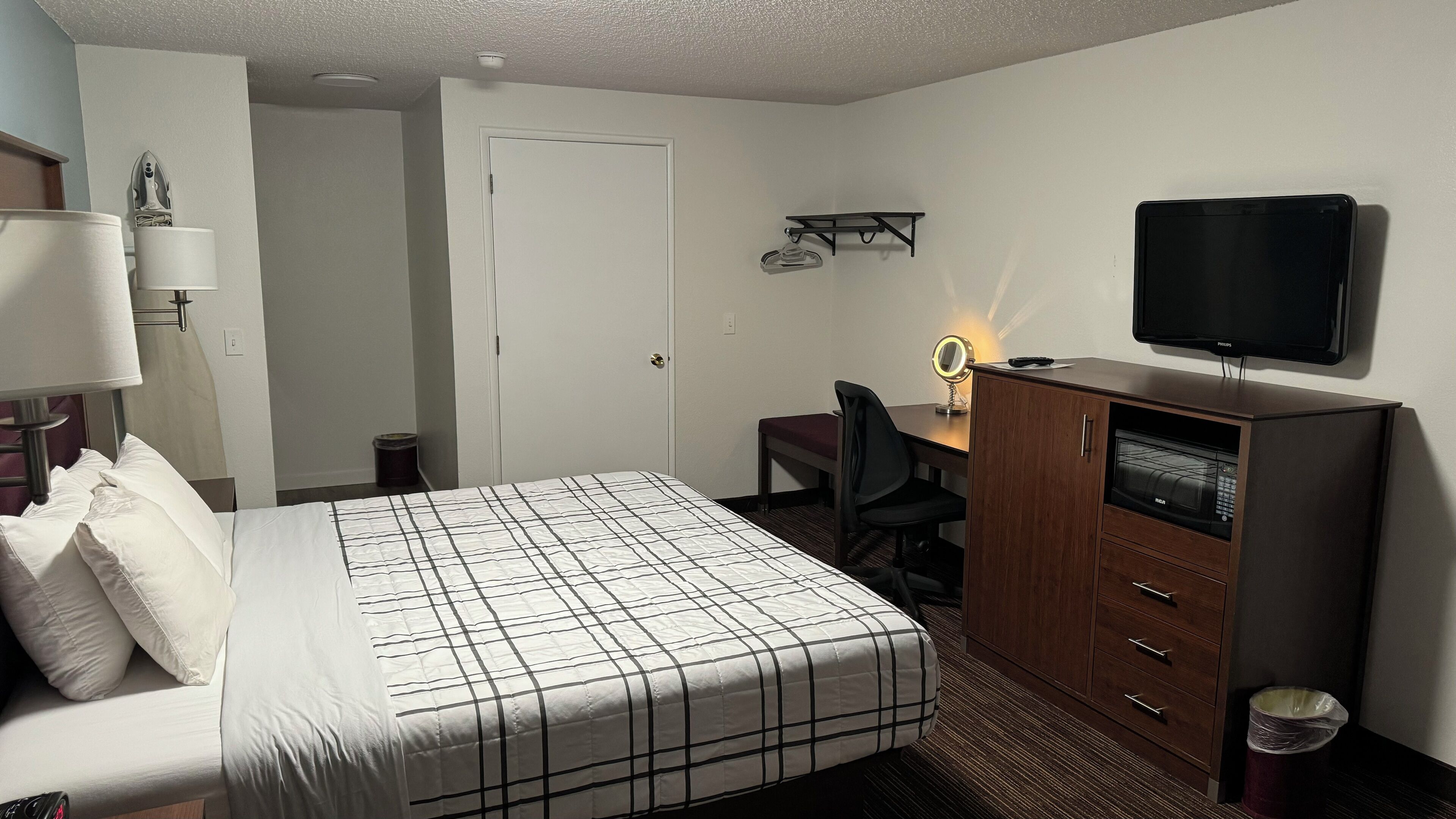 A hotel room with a bed, a desk with a chair, a television, and a mirror.