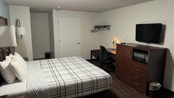 A hotel room with a bed, a desk with a chair, a television, and a mirror.