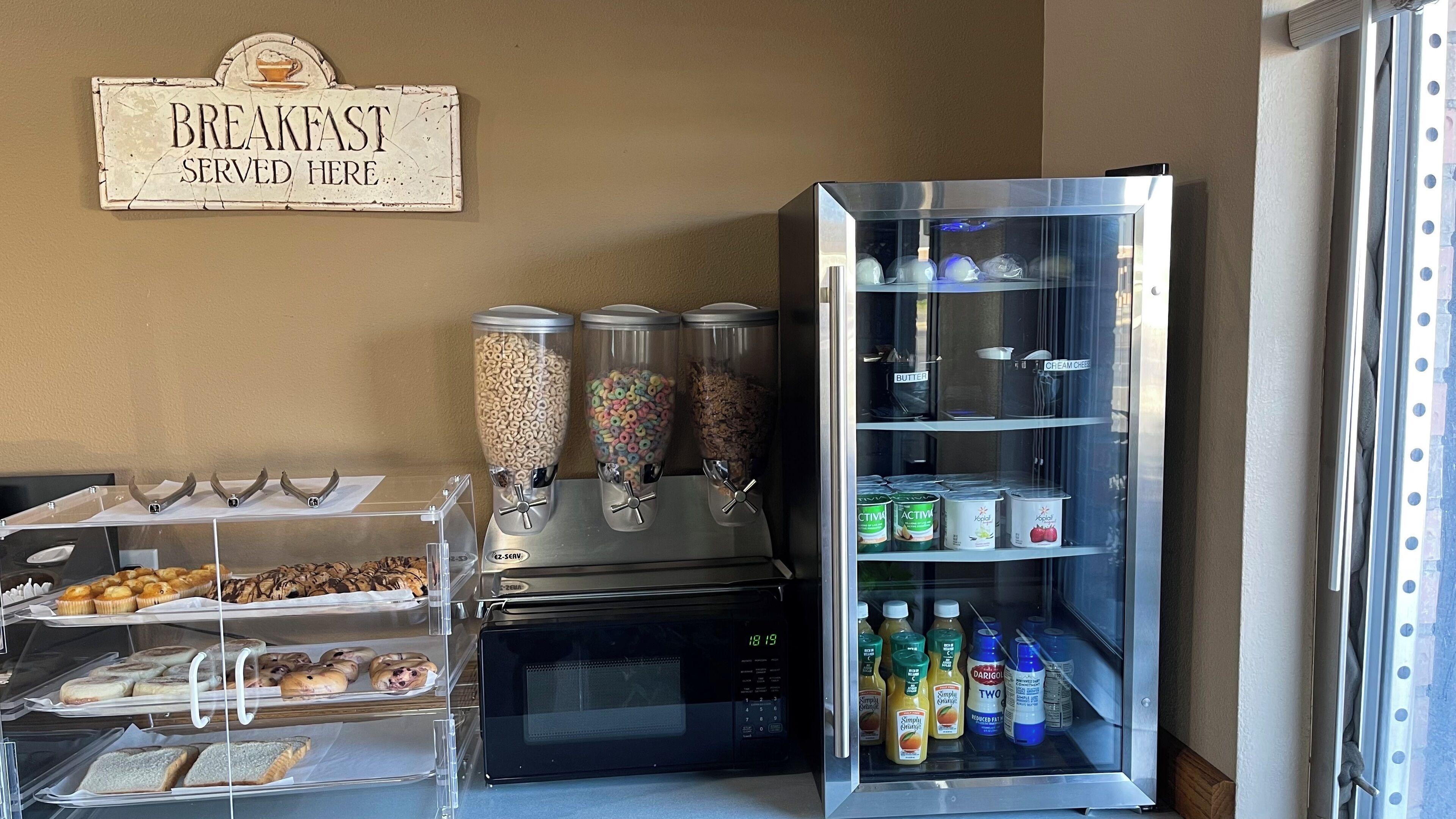 A breakfast station with cereal dispensers, a microwave, and a refrigerator stocked with beverages and spreads.
