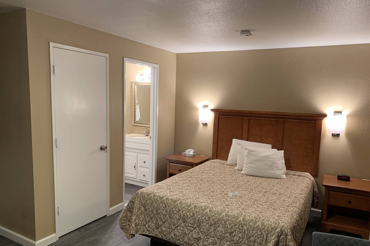A hotel room with a bed, bedside tables, a nightstand, a mirror, and a door.