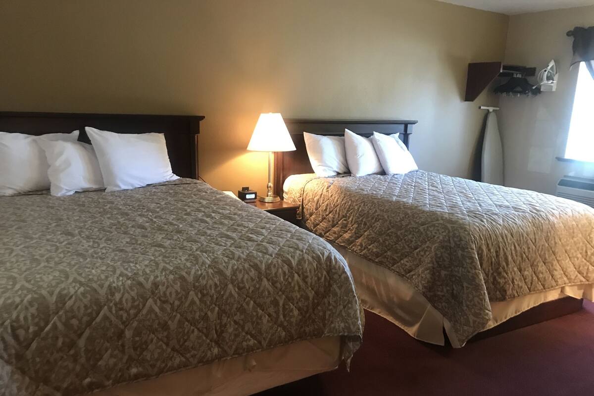 Two beds with patterned bedding, a bedside lamp, and a wall-mounted shelf with items.