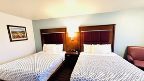 A hotel room with two beds, a nightstand, a lamp, and a framed picture on the wall.