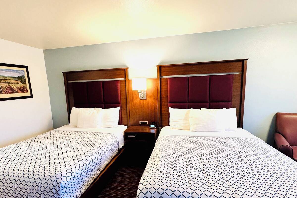 A hotel room with two beds, a nightstand, a lamp, and a framed picture on the wall.