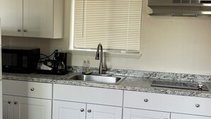 A kitchen with white cabinets, a stainless steel sink, a microwave, and a window with blinds.