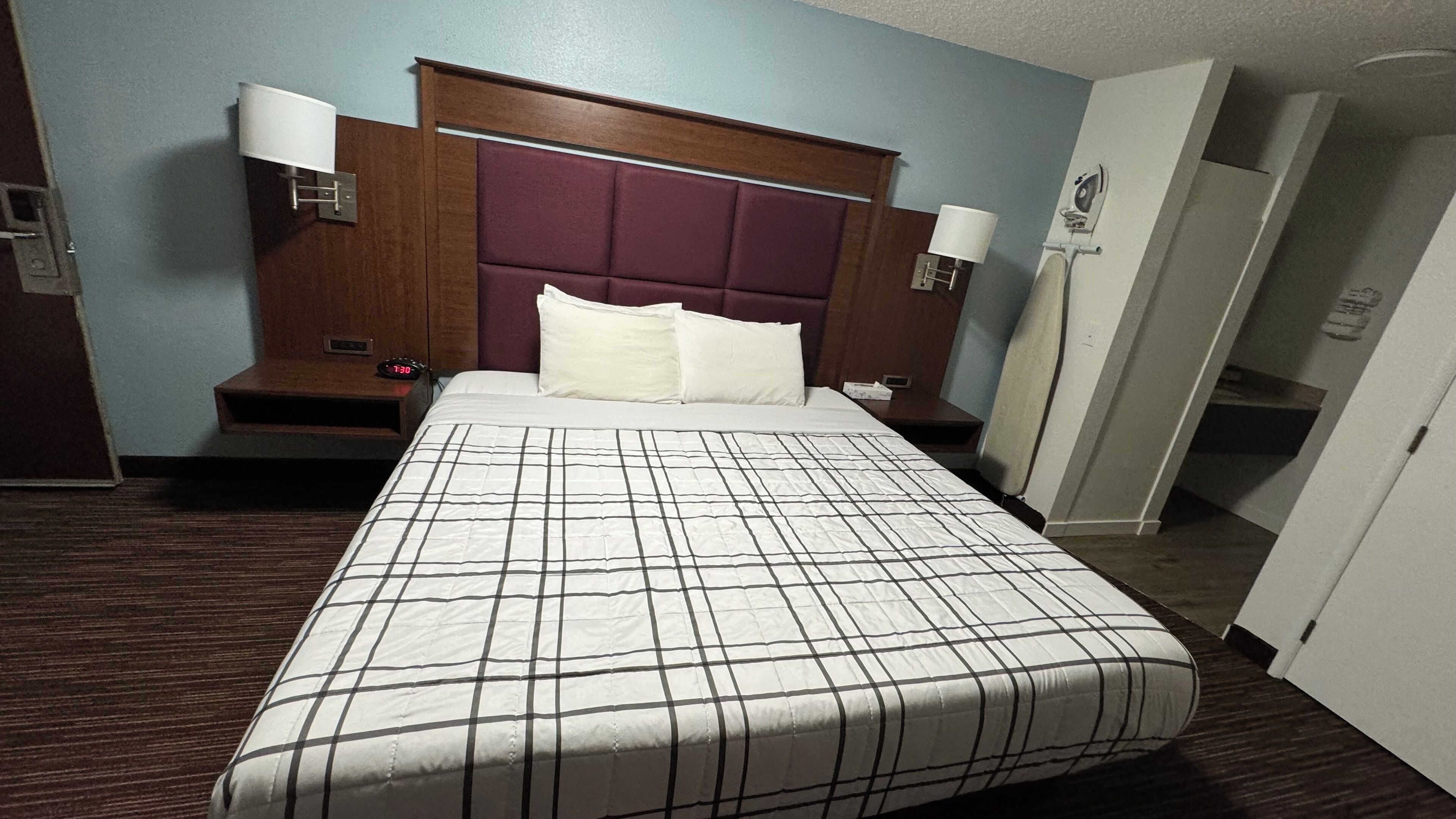 Una habitación de hotel con una cama grande, un cabecero de madera, dos mesitas de noche y una lámpara de pared.