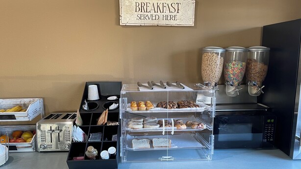 A breakfast station with a sign, a toaster, a coffee maker, and various food items.