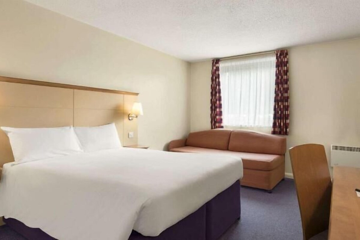Quarto de hotel com cama, sofá, escrivaninha e televisão.