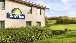 Een Days Inn gebouw met een duidelijk herkenbaar bord, omringd door verzorgde beplanting en een golfbaan op de achtergrond.