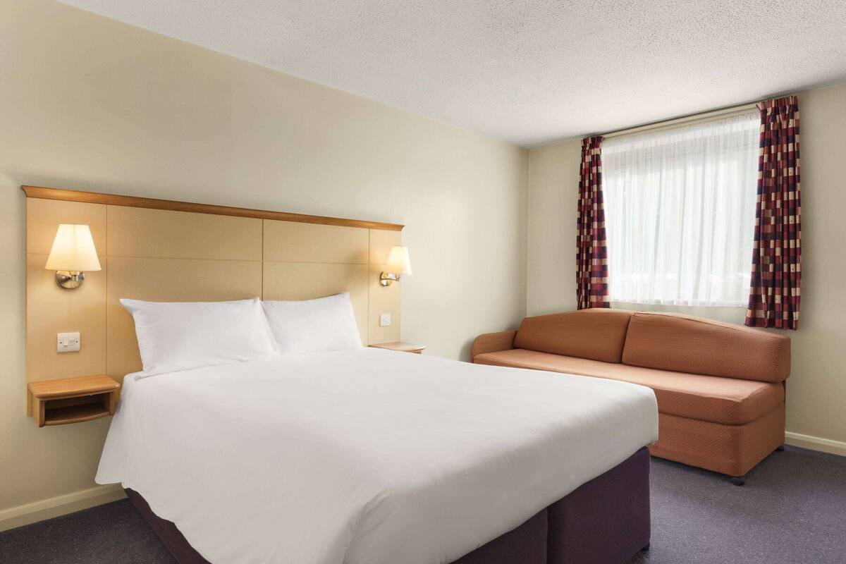 Een hotelkamer met een groot bed, twee bedlampen, een nachtkastje, een sofa en een raam met gordijnen.