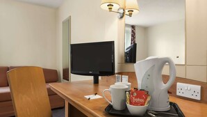 Hotelkamer met een houten bureau, een televisie, een koffiezetapparaat en een dienblad met een mok en een pak koffie.