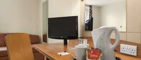 Une chambre d’hôtel équipée d’un bureau en bois, d’une télévision, d’une machine à café et d’un plateau avec une tasse et un sachet de café.