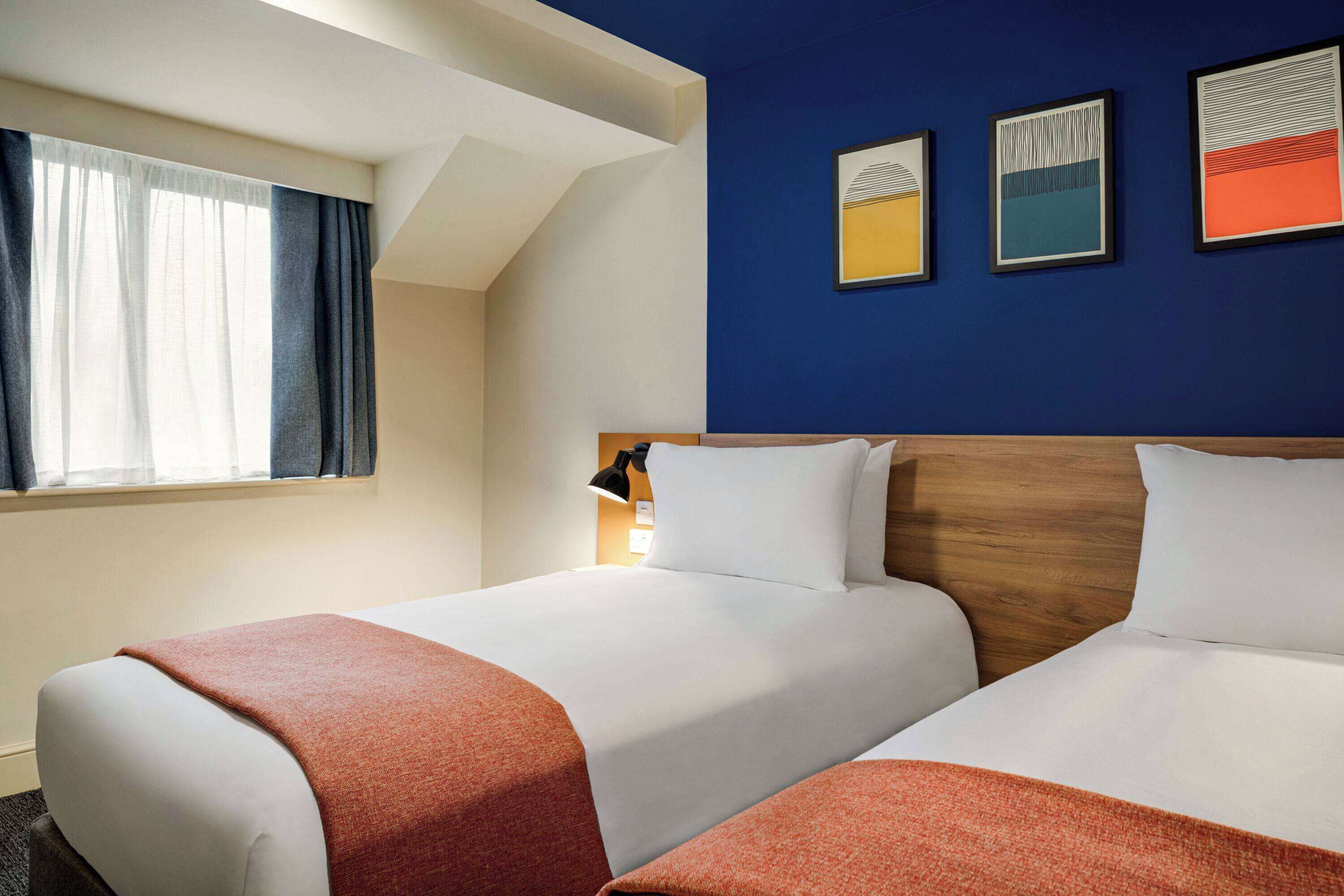 Une chambre d’hôtel avec deux lits, une tête de lit en bois et trois œuvres d’art encadrées accrochées au mur.